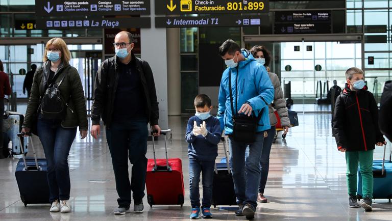 Families wear protective face masks as they walk with their luggage at Tarradellas Barcelona-El Prat Airport, after further cases of coronavirus were confirmed in Barcelona