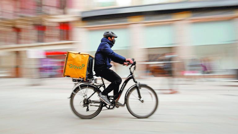 Glovo deliver rider passes by a pedestrian area in Barcelona