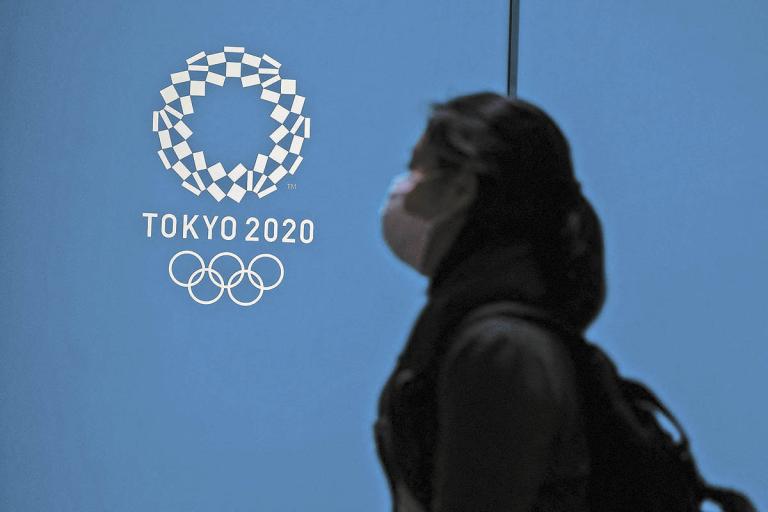 A woman walks past a logo for the Tokyo 2020 Olympic Games in Tokyo on April 13, 2021. (Photo by Charly TRIBALLEAU / AFP)