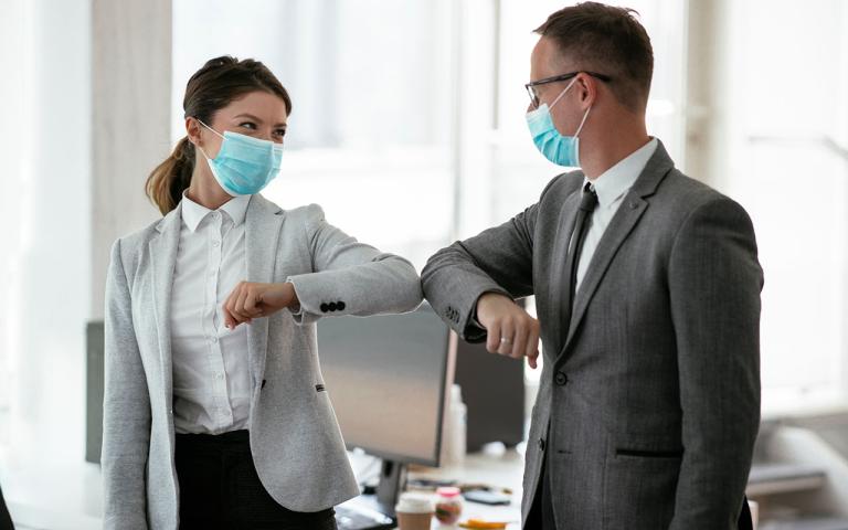 Businessman and businesswoman with medical mask in office. Greetings in Covid-19 time.