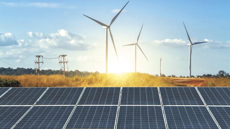 solar panels with wind turbines against mountanis landscape against blue sky with clouds