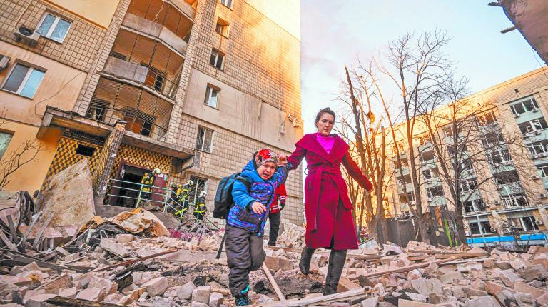 A woman with a child evacuates from a residential building damaged by shelling in Kyiv