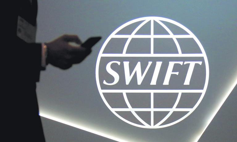 FILE PHOTO: A man using a mobile phone passes the logo of global secure financial messaging services cooperative SWIFT at the SIBOS banking and financial conference in Toronto