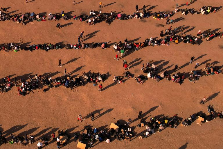 Migrants stand near the border wall, as seen from Ciudad Juarez