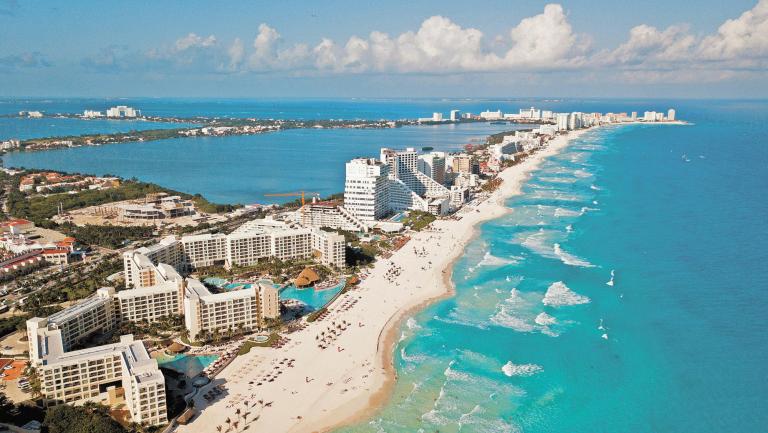 Aerial view of Cancun, Mexico showing luxury resorts and blue turquoise beach. showing people parasailing, swimming and tanning on the beach.