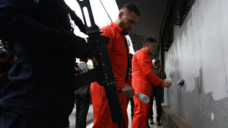 Miembros de la Policía Militar de Orden Público (PMOP) custodian a reclusos mientras borran grafitis alusivos a las pandillas Barrio 18 y Mara Salvatrucha (MS-13) . Foto: AFP