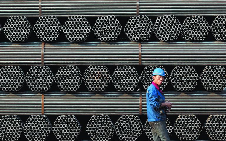 File photo of a worker walking past a pile of steel pipe products in China