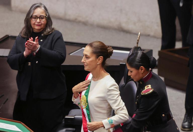 La nueva presidenta de México, Claudia Sheinbaum, es asistida mientras se coloca la banda presidencial, Norma Piña, presidenta de la Suprema Corte de Justicia aplaude durante la ceremonia.