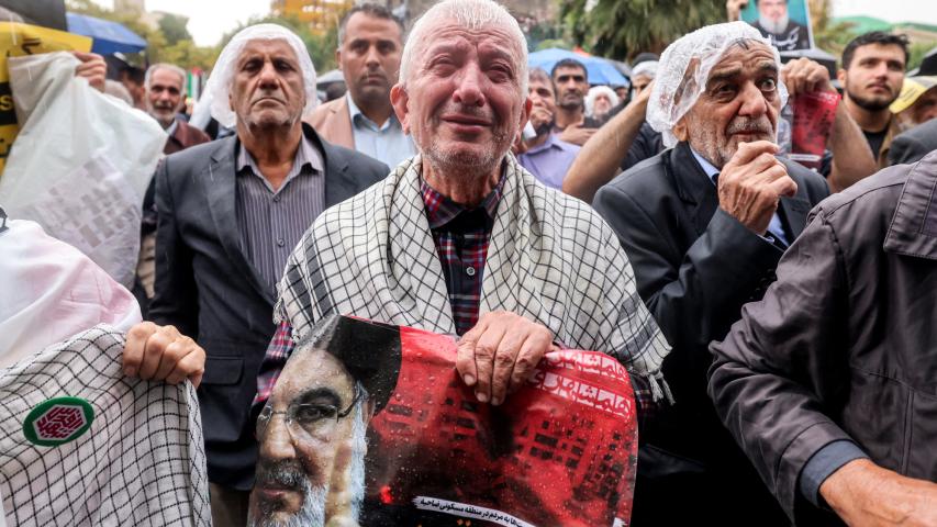 Un hombre llora mientras sostiene un cartel que dice "cruzando una línea roja" en persa junto a una imagen de Hassan Nasrallah.