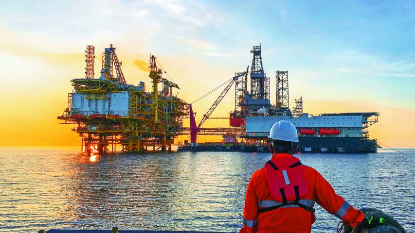 Oil and gas industry. Marine crew standing on supply vessel looking oil and gas platform during sunrise.