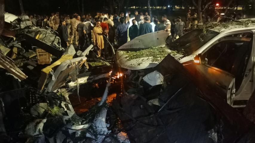 La gente se encuentra cerca de los restos de los vehículos mientras se reúnen después de una explosión cerca del Aeropuerto Internacional Yiná en Karachi.