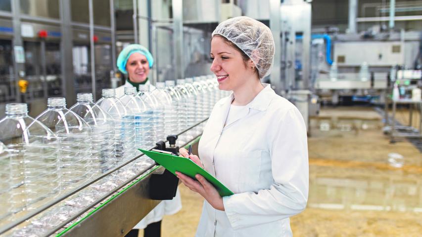 Female workers in bottling factory checking water bottles before shipment. Inspection quality control.