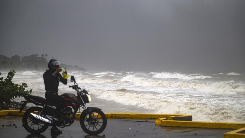 A motorcyclist takes photos at the boardwalk during the passage of tropical storm Sara in La Ceiba, Honduras, on November 15, 2024. - Honduras' President Xiomara Castro said emergency services had been activated to deal with "damage already caused by the rains," warning that Sara's impacts "could become a catastrophic event." (Photo by ESAU OCAMPO / AFP)