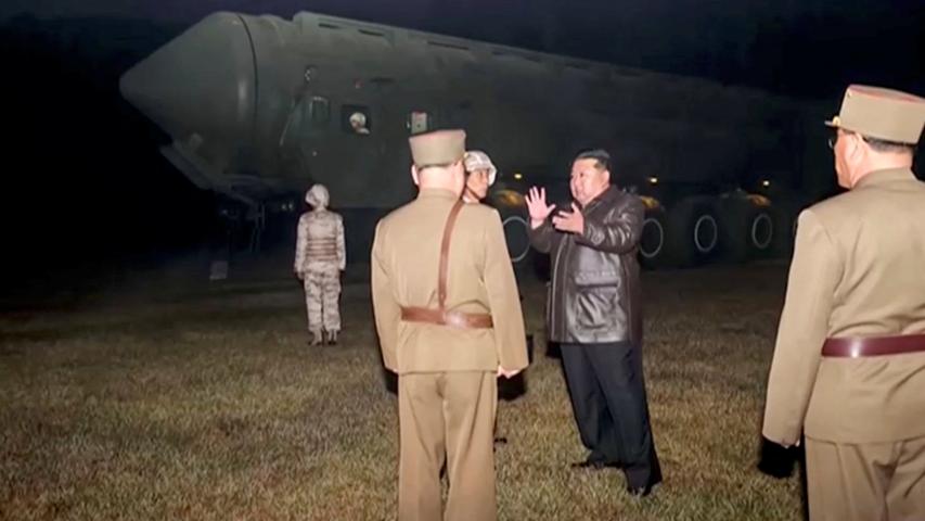 El líder norcoreano Kim Jong Un y funcionarios militares se encuentran junto a lo que dicen es un vehículo lanzamisiles móvil.