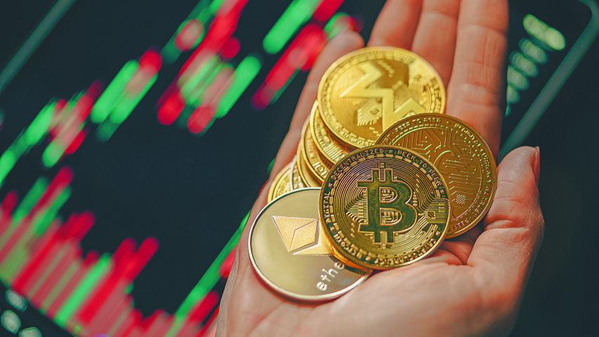 Hand holding various gold cryptocurrency coins with candle stick graph chart and digital background. Bitcoin, Ethereum, Litecoin, dogecoin.