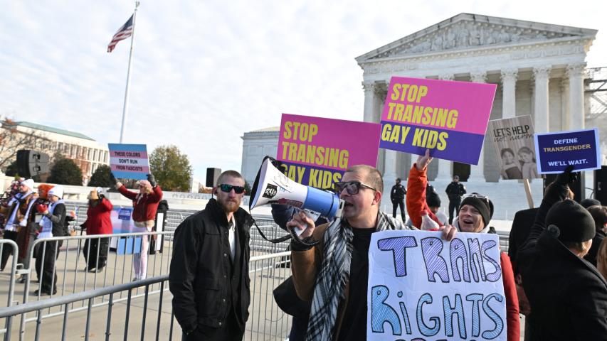 Varias personas sostienen carteles frente a la Corte Suprema de Estados Unidos durante los alegatos orales sobre si los estados pueden prohibir ciertos tratamientos médicos de transición de género para jóvenes.