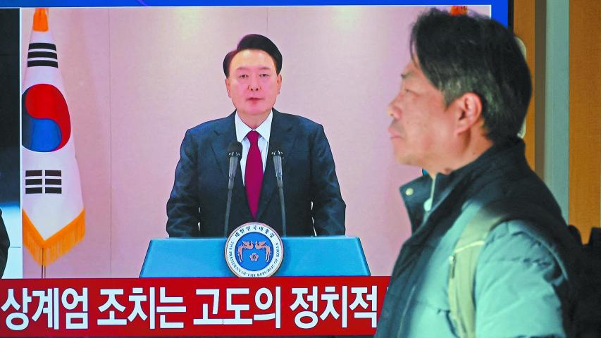 A person stands by a TV screen broadcasting South Korean President Yoon Suk Yeol delivering an address to the nation, at a railway station in Seoul, South Korea, December 12, 2024. REUTERS/Kim Hong-Ji