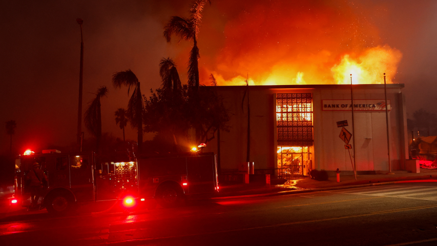 Humo y llamas se elevan desde un edificio del Bank of America, mientras los vientos que alimentan los devastadores incendios forestales en el área de Los Ángeles obligan a la gente a evacuar, en Eaton, en Altadena, California.