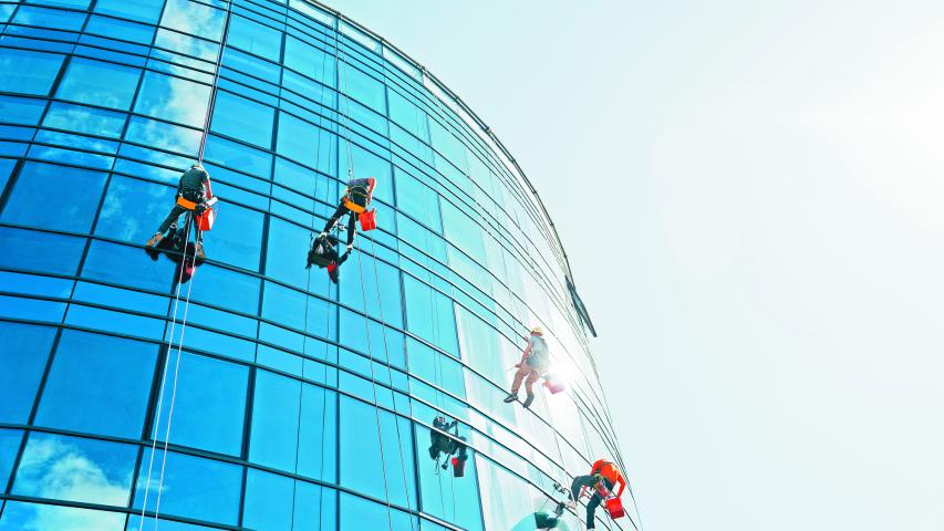 Industrial climbers cleaning blue windows outside building.