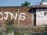 View of a bullet-riddled wall bearing the initials of the criminal group Cartel Jalisco Nueva Generacion (CJNG) at the entrance of the community of Aguililla, state of Michoacan, Mexico, on April 23, 2021. The municipality of Aguililla is being threatened due to the confrontation of organized crime groups called the Jalisco Nueva Generacion Cartel (CJNG) and the Michoacan Family (now called Viagras). (Photo by ENRIQUE CASTRO / AFP)