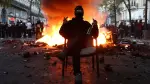 Un manifestante enmascarado se sienta en una silla frente a una barricada en llamas que bloquea una calle en medio de enfrentamientos durante una jornada de manifestaciones contra el costo de la vida.
