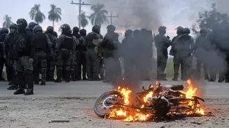 A motorcycle burns near police officers during clashes with anti-government demonstrators amid an operation to clear a road blockade in San Julian, Santa Cruz department, Bolivia, on June 6, 2026. Bolivia has faced days of demonstrations and road blockades amid growing political tensions and shortages affecting different regions of the country. (Photo by Rodrigo URZAGASTI / AFP)