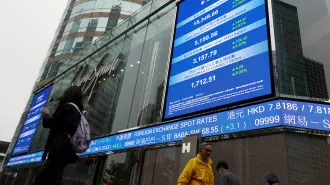 Personas pasan frente a pantallas que muestran el índice bursátil Hang Seng y los precios de las acciones en el exterior de Exchange Square en Hong Kong.