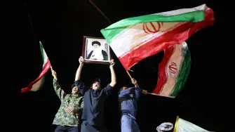 Chiítas iraquíes gritan consignas mientras portan un retrato del líder supremo de Irán, el ayatolá Ali Khamenei, y ondean banderas iraníes durante una protesta contra los ataques estadounidenses.