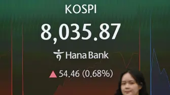 A currency dealer walks past a screen showing South Korea's benchmark stock index (KOSPI) as it breaks 8,000 points in a foreign exchange dealing room at the Hana Bank headquarters in Seoul on May 15, 2026. South Korea's benchmark Kospi index topped 8,000 points for the first time on May 15, buoyed by an artificial intelligence-driven boom in the country's semiconductor industry. (Photo by Jung Yeon-je / AFP)