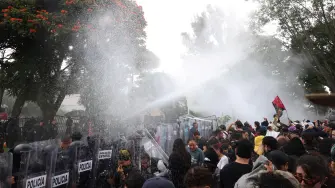 Protesters stand near state riot police as a water cannon is used during clashes at a demonstration demanding clean water, after weeks of residents' complaints about discolored and foul-smelling water in parts of the metropolitan area, outside Casa Jalisco, the official residence of the state governor, in Guadalajara, Mexico, October 11, 2026. REUTERS/Stringer