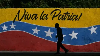 Un hombre pasa junto a un mural que representa la bandera nacional venezolana y que dice "¡Viva la patria!".
