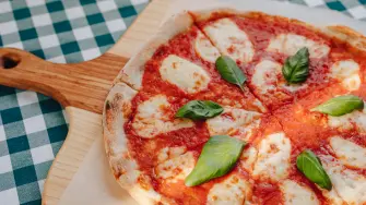 Neapolitan pizza on a cream sauce with ham, cheese, arugula, basil, tomatoes sprinkled with cheese on a wooden board on a tablecloth in a cell with a place for text
