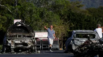 Personas caminan en el estacionamiento de un supermercado donde varios vehículos fueron consumidos por las llamas días después de una serie de bloqueos y ataques del crimen organizado tras un operativo militar en el que fue asesinado el líder del CJNG, "El Mencho".