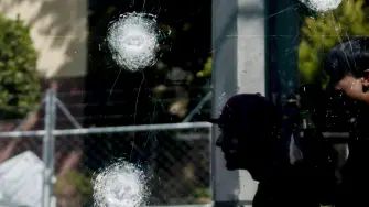 Young men walk past teh window of a police station with bullet impacts in Guadalajara, Jalisco, Mexico, on February 23, 2026, a day after clashes. Mexico has deployed 10,000 troops to quell clashes sparked by the killing of the country's most-wanted drug lord, Nemesio "El Mencho" Oseguera, leader of the Jalisco New Generation Cartel (CJNG), that have claimed dozens of lives, officials said on February 23. News of his death triggered spasms of violence, with cartel members blocking roads in 20 states and torching vehicles and businesses. (Photo by Ulises RUIZ / AFP)