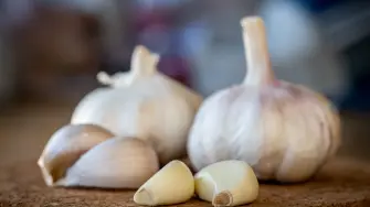 A closeup of garlic bulb and cloves on a round cork board