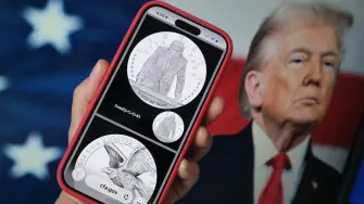 This illustration photo created on March 19, 2026 in Los Angeles shows a phone displaying the commemorative gold coin design marking America's 250th anniversary, approved by the United States Commission of Fine Arts, in front of a computer screen showing US President Donald Trump. An advisory commission hand-picked by President Donald Trump has approved the design of a commemorative gold coin featuring his image, officials said Thursday, in a move slammed by Democratic opponents. The US Commission of Fine Arts declined to comment when asked by AFP after several media outlets showed the proposed design in reporting on the approval. (Photo by Chris DELMAS / AFP) / -- IMAGE RESTRICTED TO EDITORIAL USE - STRICTLY NO COMMERCIAL USE --