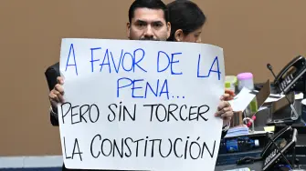 Deputy of the Nationalist Republican Alliance (ARENA) party Francisco Lira shows a sign that reads "In favor of the penalty, but without violating the Constitution" during the ratification of the constitutional reform to approve life imprisonment and extend the emergency regime to reach four years at the Legislative Assembly in San Salvador on March 26, 2026. (Photo by Marvin RECINOS / AFP)