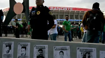 A Mexican police officer stands guard past a demonstration with signs of disappeared people ahead of the inauguration of Banorte Stadium (formerly known as Azteca), for a friendly match between Mexico and Portugal, in Mexico City on March 28, 2026. (Photo by YURI CORTEZ / AFP)