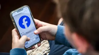 This photo taken on October 24, 2025 shows a 14-year-old boy posing at his home near Gosford as he looks at the Facebook page on his mobile phone. Popular social media website Reddit and streaming giant Kick will be added to a list of websites banned for under-16s in Australia from next month, Canberra said on November 5. Australia will from December 10 force social media platforms including Facebook, Instagram and Tiktok to remove users under the age of 16, slapping hefty fines of up to Aus$49.5 million (US$32 million) if they fail to do so. (Photo by David GRAY / AFP)