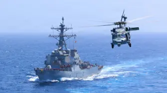 El USS Donald Cook (DDG 75) transita por el mar Arábigo mientras un MH-60S Sea Hawk vuela cerca.