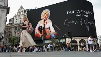 Unas personas pasan junto a un homenaje a la cantante estadounidense de música country Dolly Parton en Piccadilly Circus, un día después del anuncio de su fallecimiento a los 80 años, en Londres.