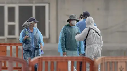 Pasajeros turcos del crucero MV Hondius, con bandera holandesa y afectado por el hantavirus, conversan con personal con trajes de protección biológica al desembarcar en el puerto industrial de Granadilla de Abona, en la isla de Tenerife.