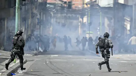 Agentes antidisturbios disparan gases lacrimógenos mientras manifestantes corren.