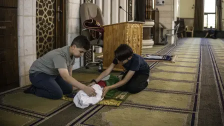 Kinan Abou Haikal (izquierda), hermano mayor del bebé de siete meses Sam Fahd Abou Haikal, se sienta junto a su cuerpo en la mezquita Abou Heisheh.