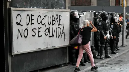 Una anciana pasa junto a agentes antidisturbios que se enfrentan a manifestantes durante una concentración en conmemoración del 57 aniversario de la masacre estudiantil de Tlatelolco de 1968 en la Ciudad de México, el 2 de octubre de 2025.