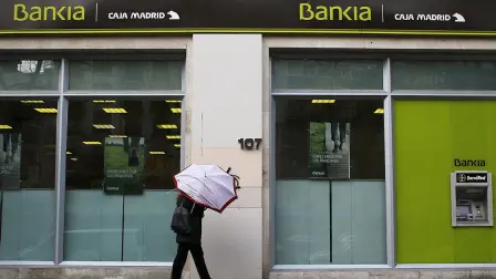 A couple walks with a broken umbrella past a branch of Spain
