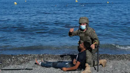 Un soldado español ayuda a un ciudadano marroquí en la playa El Tarajal, cerca de la valla entre la frontera hispano-marroquí, después de que miles de migrantes cruzaran esta frontera durante los últimos días, en Ceuta. Foto: Reuters.