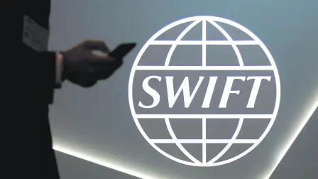 FILE PHOTO: A man using a mobile phone passes the logo of global secure financial messaging services cooperative SWIFT at the SIBOS banking and financial conference in Toronto