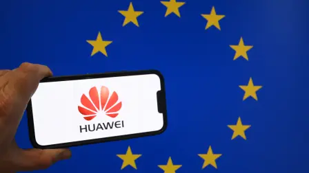 This illustration photograph taken in Brussels on March 13, 2025 shows Chinese telecom giant Huawei logo displayed on a smartphone in front of an European Union flag. Belgian police raided several addresses in the country as part of a probe into alleged corruption 