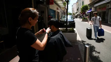 Una peluquera corta el pelo a una clienta en la calle debido a la falta de luz en su peluquería, tras un importante apagón, durante el 78º Festival de Cine de Cannes.